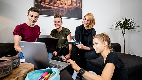 our young adults are gathered around a laptop. The group appears engaged and collaborative, discussing ideas and sharing notes. 