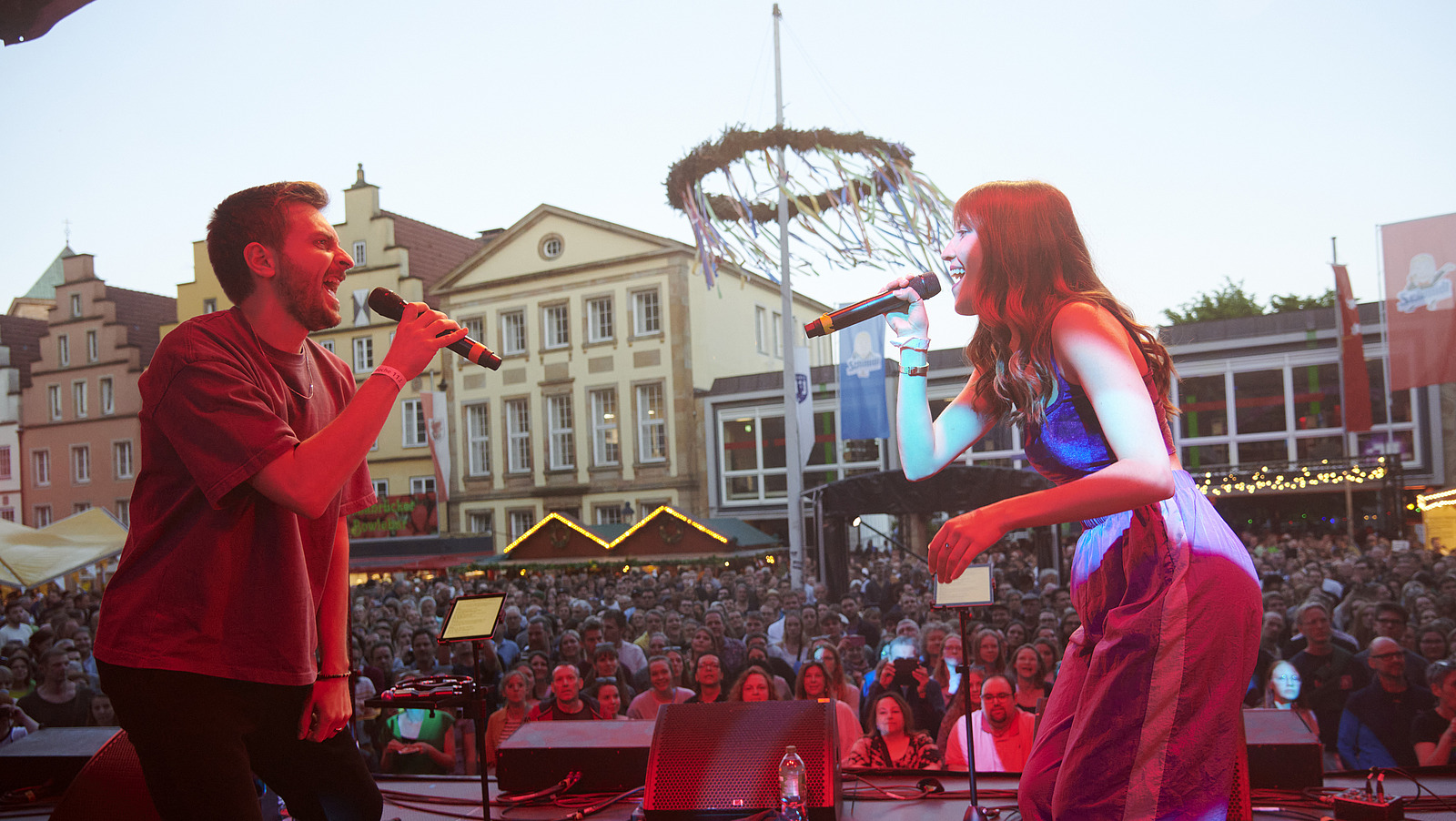 Two people stand opposite each other on stage and look at each other while singing