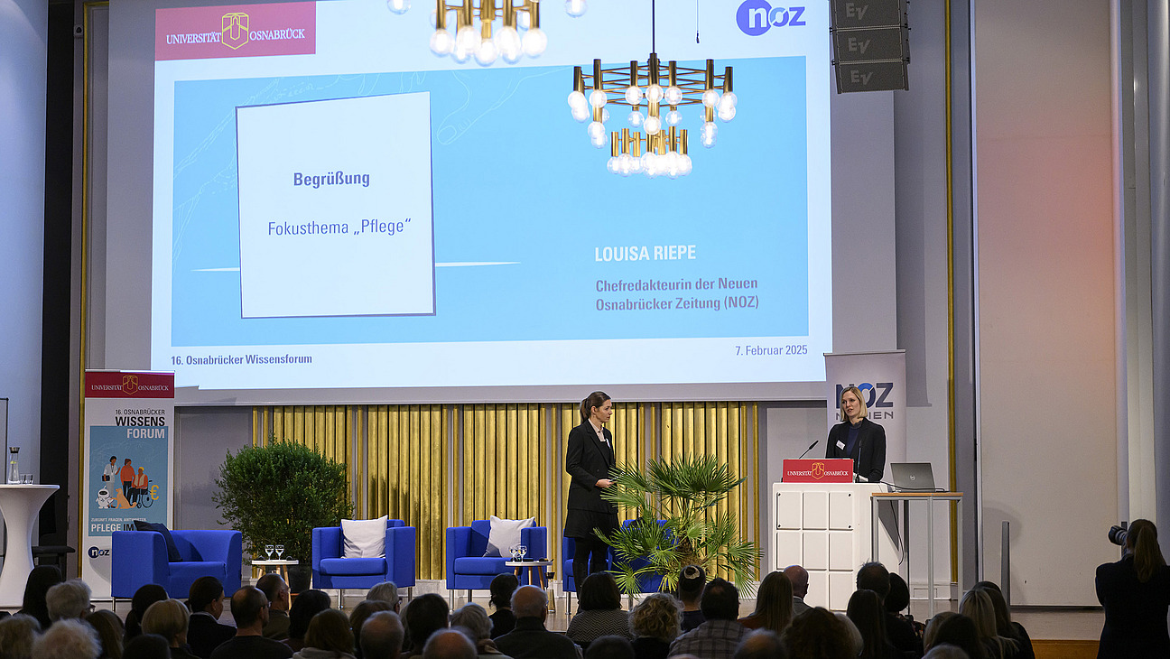 Two women stand on the podium and welcome the audience.