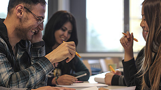 Three international students working together at a table and laughing.