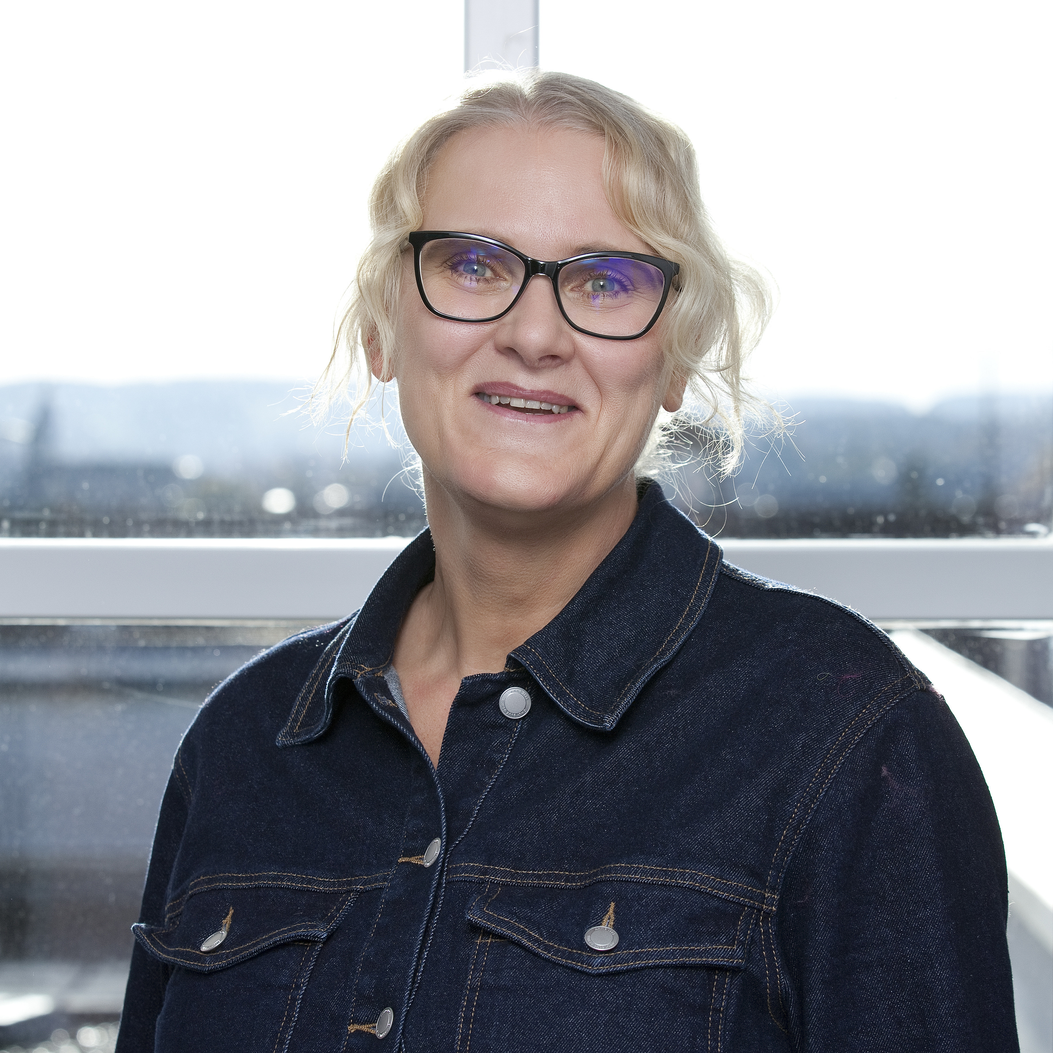 Portraitfoto einer Frau mit Brille und hochgestecktem, blondem Haar