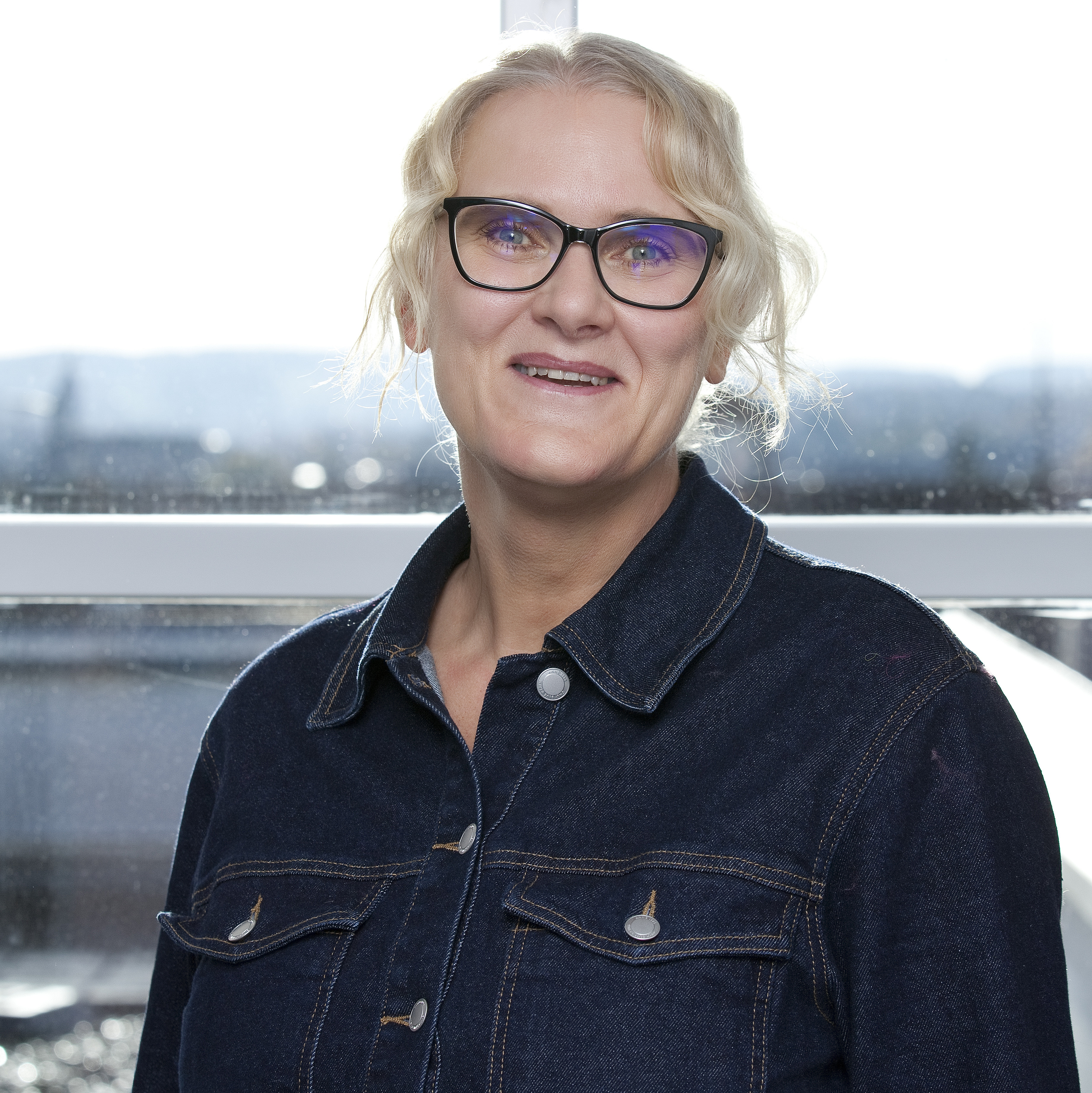 Portraitfoto einer Frau mit Brille und hochgestecktem, blondem Haar