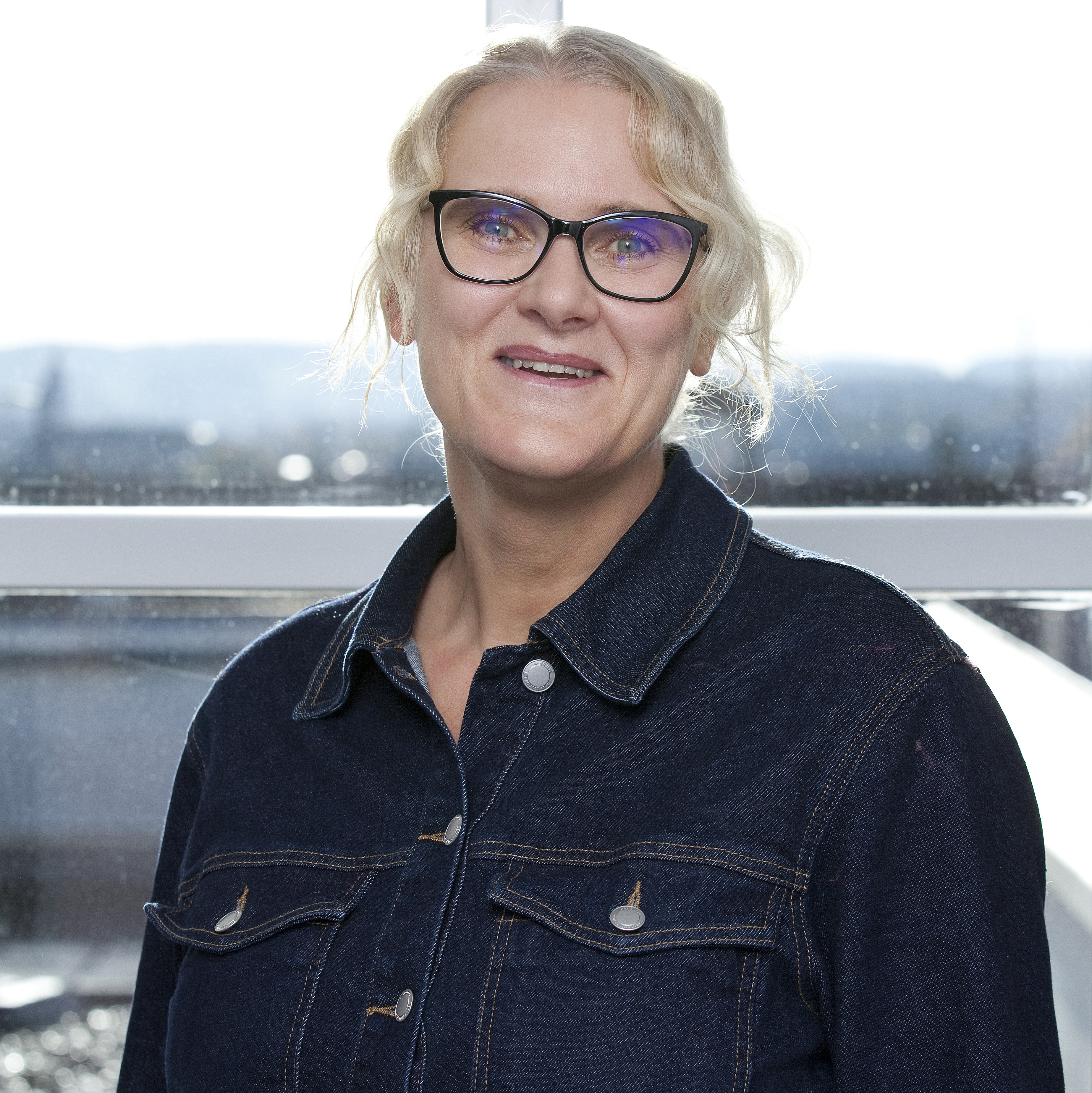 Portraitfoto einer Frau mit Brille und hochgestecktem, blondem Haar