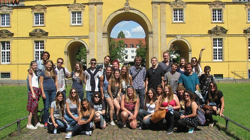 A group of international students and their chaperones from the International Office stand together in front of the entrance to Osnabrück University.