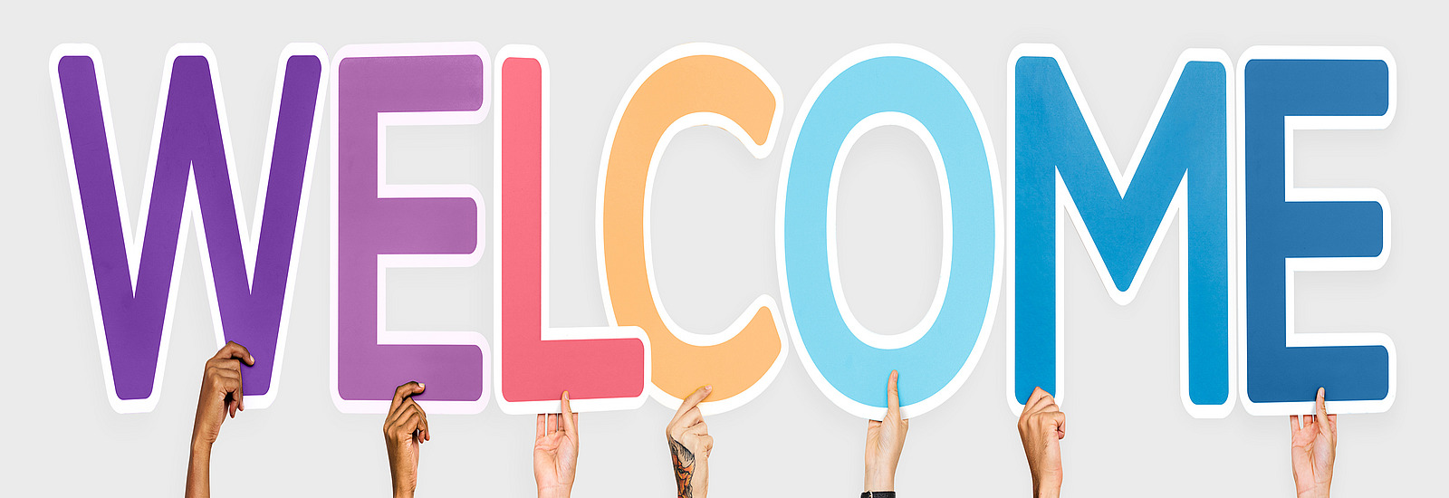 Different hands hold up various colored letters that together form the word “WELCOME”.