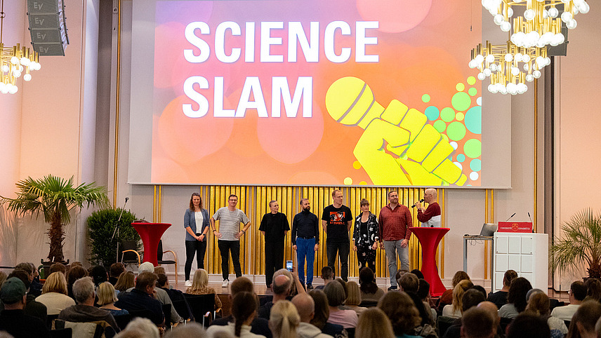 Eine Bühne mit dem Schriftzug "SCIENCE SLAM" und einer Gruppe von Rednern.