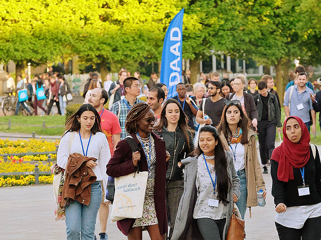 Many young people are walking through the castle park to a DAAD event for which banners have been put up. Everyone is wearing business cards on a pendant around their neck.