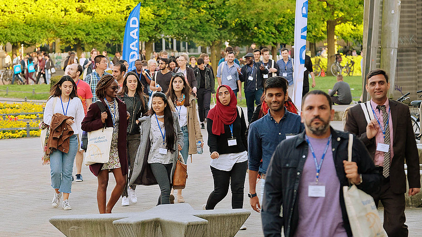 Many young people are walking through the castle park to a DAAD event for which banners have been put up. Everyone is wearing business cards on a pendant around their neck.