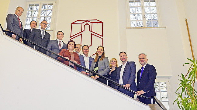 Numerous people on a staircase, in the background the logo of Osnabrück University