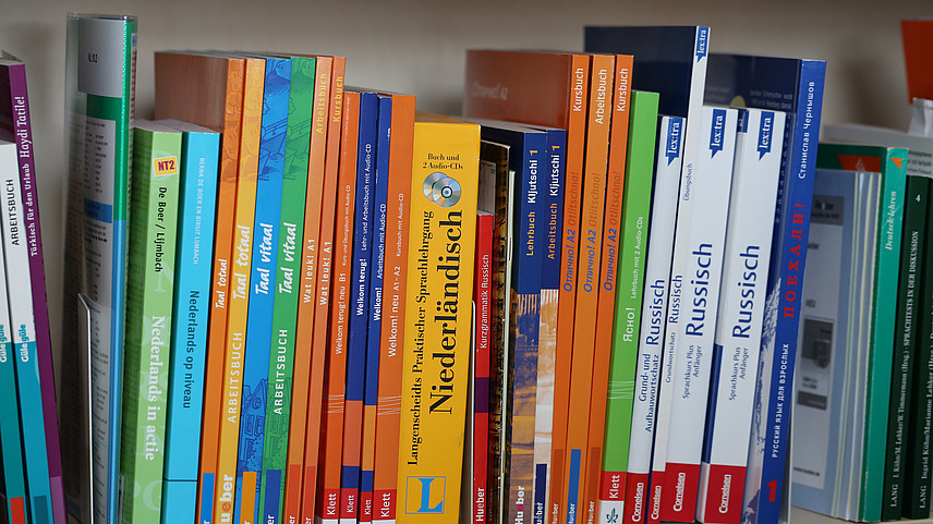 Different colored books for language learning are on a bookshelf.