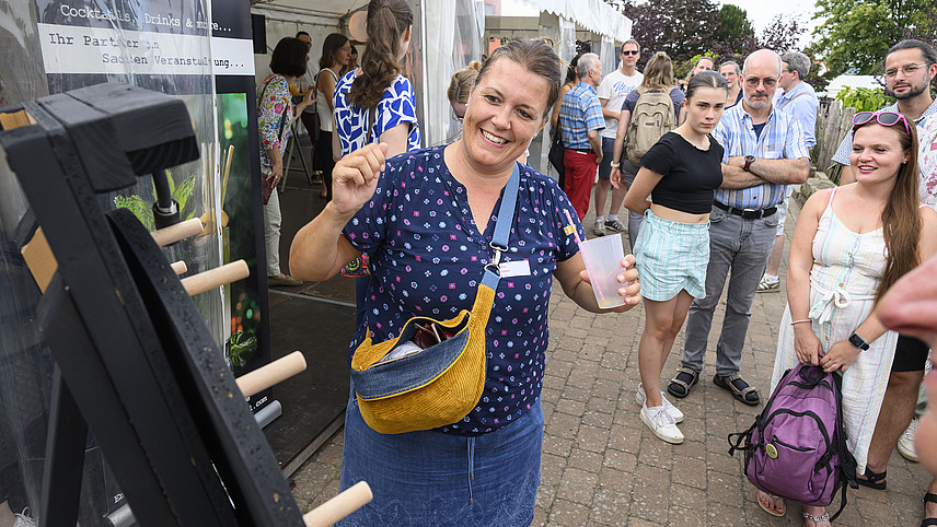 A cheerful woman spins a wheel of fortune in front of spectators.