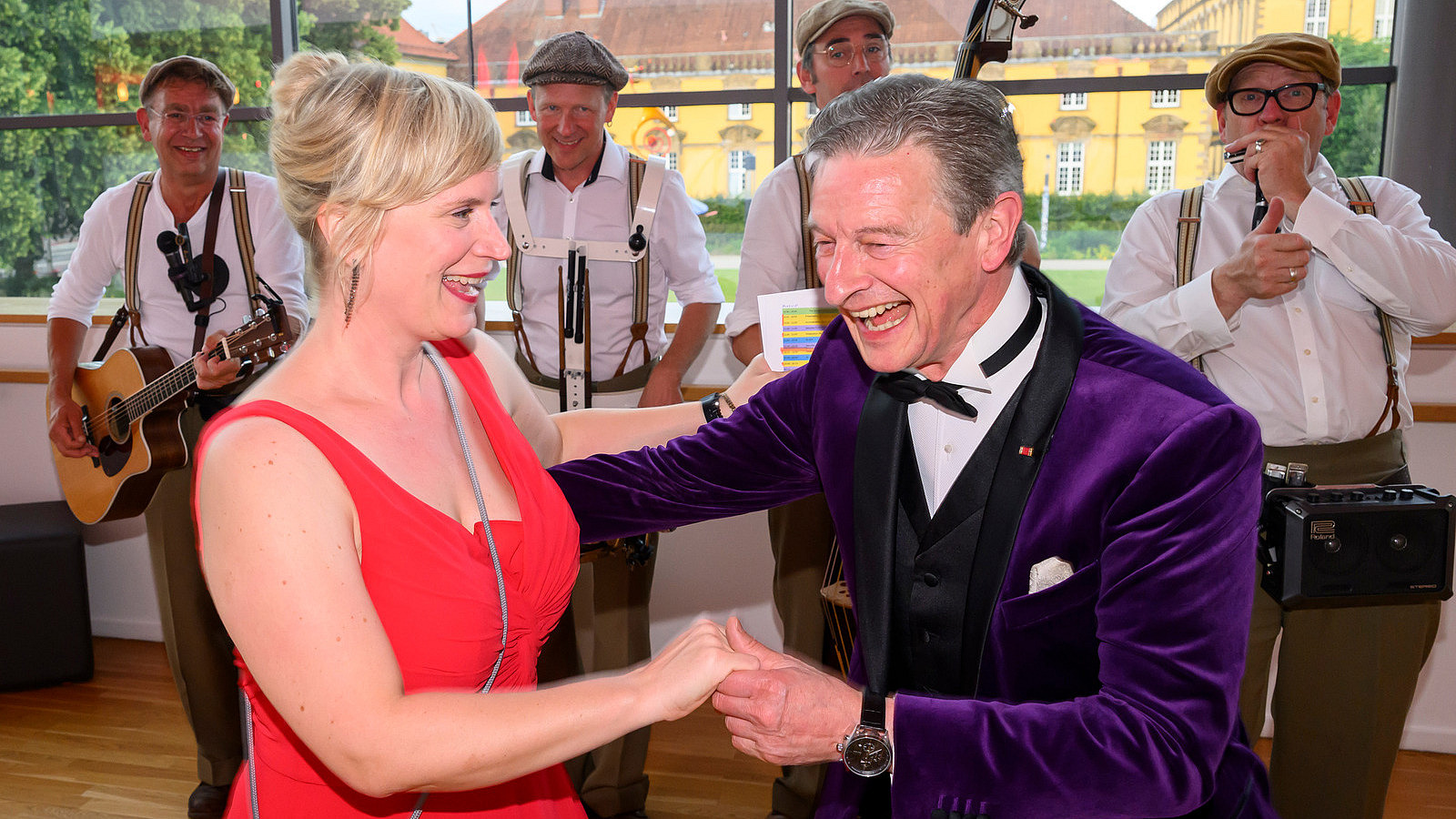 Presenters Nele Kießling and Michael Hull stand laughing and dancing in front of the marching band