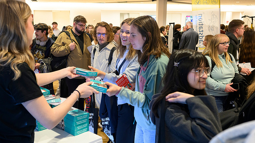 Mehrere Personen an einem Infostand bekommen ein Give-away überreicht