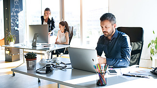 Drei Geschäftsleute am Arbeitsplatz. Zwei Frauen und ein Mann sitzen im Büro und arbeiten zusammen.