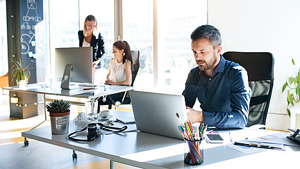 Drei Geschäftsleute am Arbeitsplatz. Zwei Frauen und ein Mann sitzen im Büro und arbeiten zusammen.