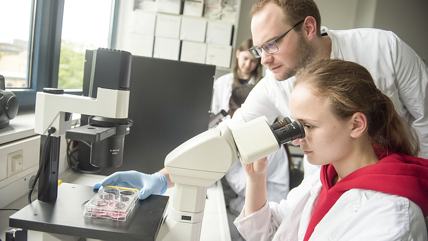 A student and a man in a white coat at a microscope