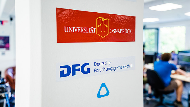 A pillar with the logo of Osnabrück University and the German Research Foundation, DFG.