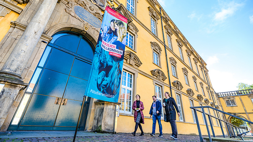 Eine Werbefahne mit dem Slogan "Herzlich Willkommen. Uni Osnabrück #studierenleben" vor dem Eingang des Schlosses.