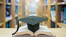 graduation cap over open Books on Library room