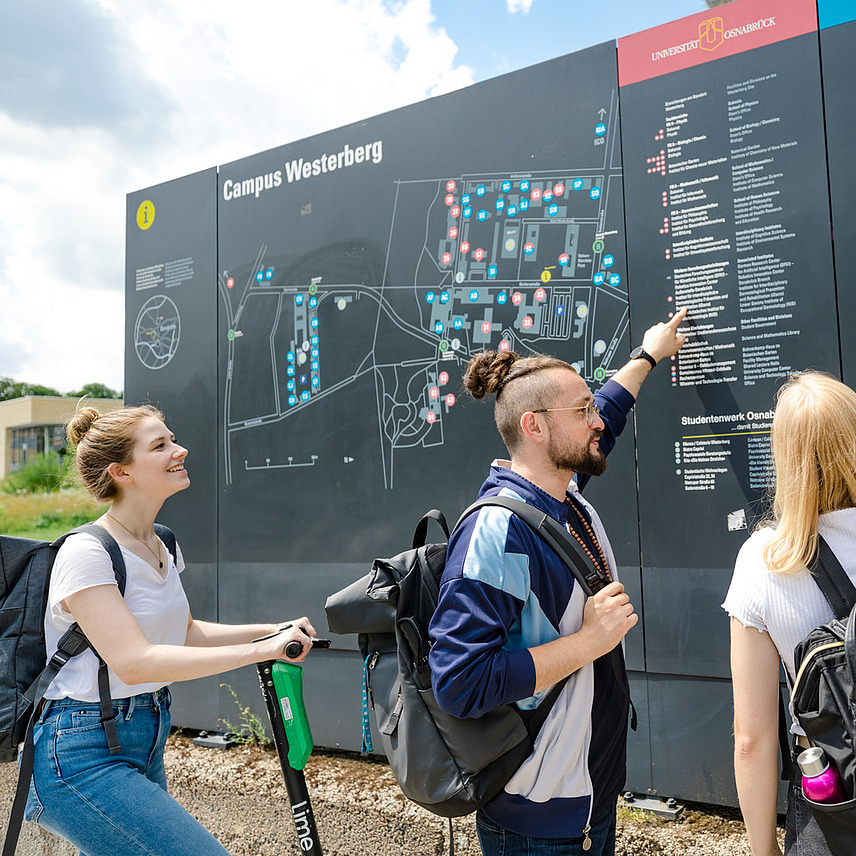 Ein paar Studierende zeigen mit dem Finger auf Gebäude auf einem großen Lageplan vom Westerberg