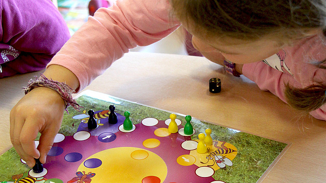 a child playing a board game. In the background you can see other children