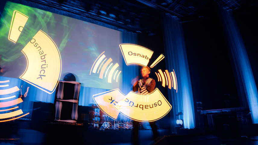 Two people on stage juggling to create the Osnabrück town sign as a laser hologram