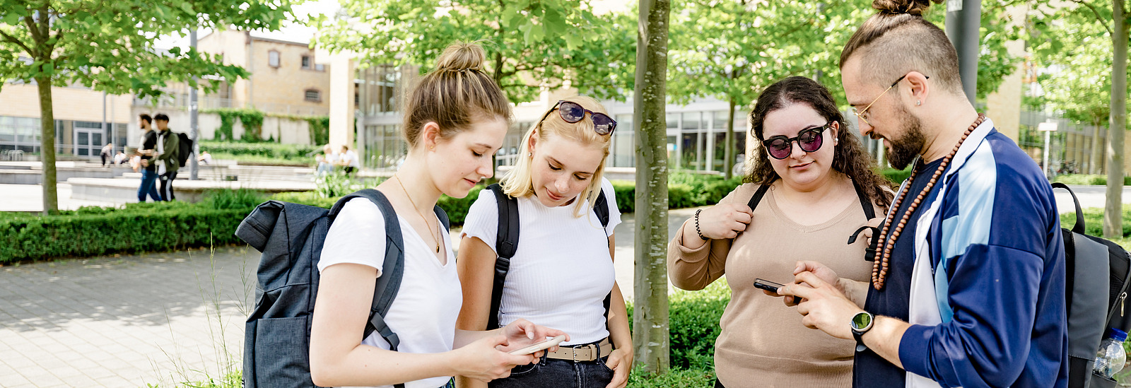 Four students look at their cell phones together. You can just make out the canteen in the background.