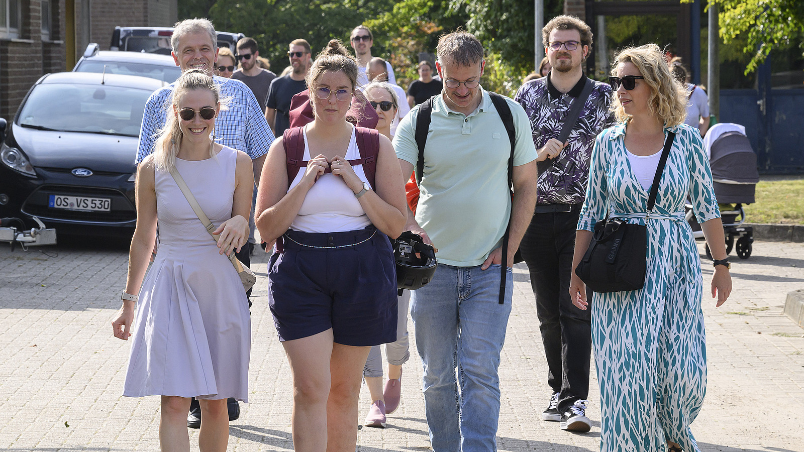 Several cheerful people walk towards the camera, wearing summer clothes.