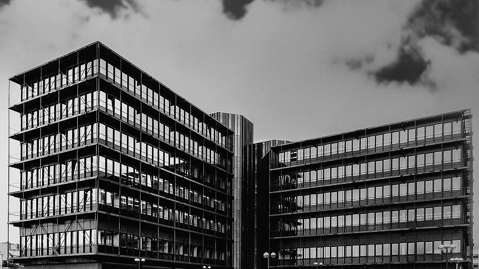 Schwarzweiß-Aufnahme des Gebäudes, auf dem Parkplatz Fahrzeuge aus den 1970er Jahren