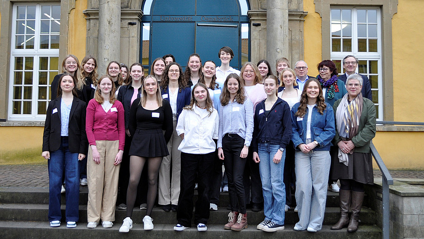 Eine Gruppe junger Frauen steht für ein Gruppenfoto vor einem großen gelben Gebäude