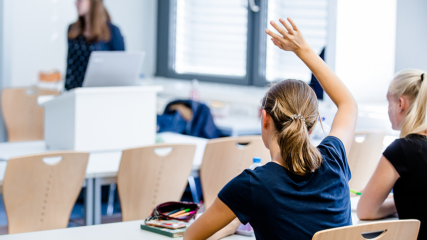 Eine Studentin in einem Seminarraum hebt die Hand zur Meldung.