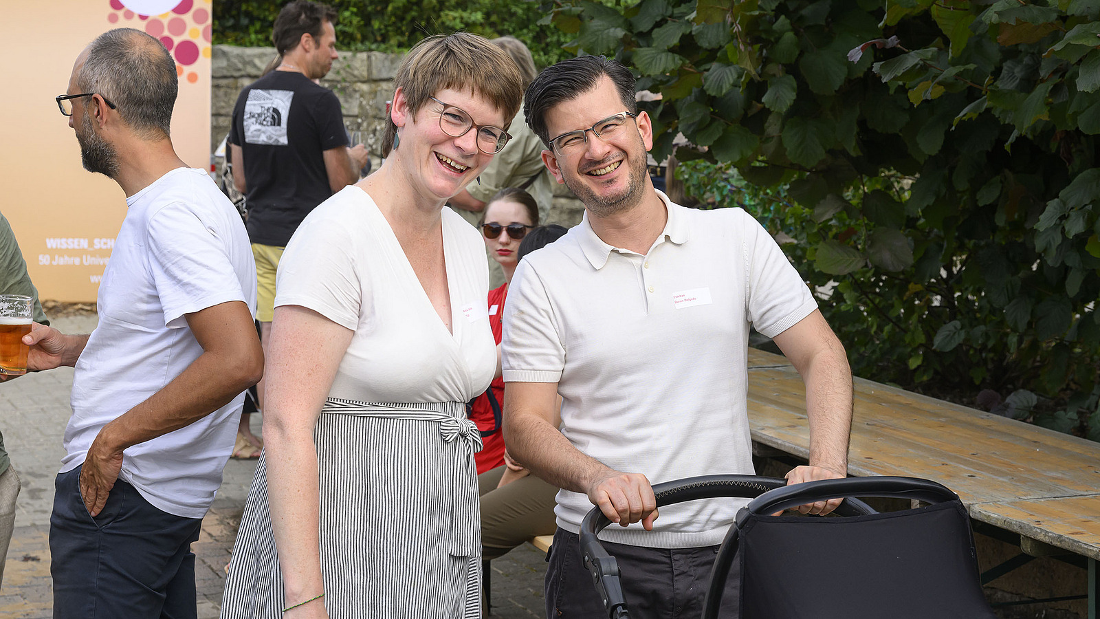 A woman and a man with a baby carriage laugh into the camera.