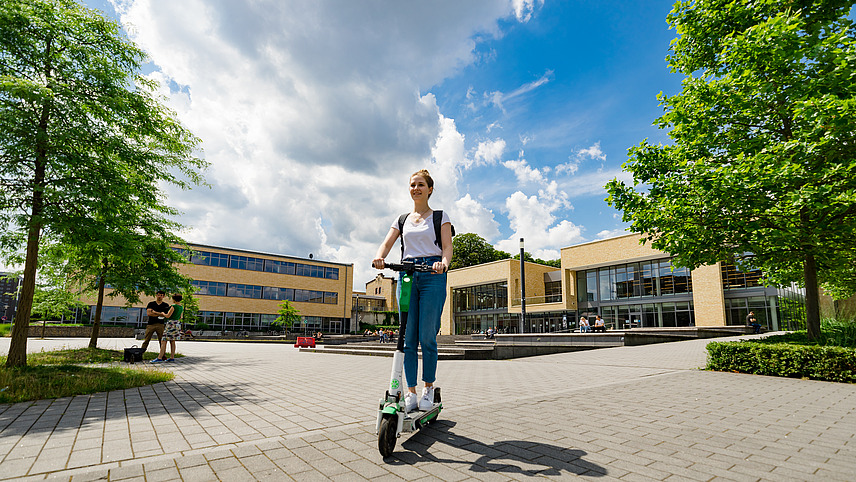 Eine Studentin fährt E-Roller auf dem Platz vor der Mensa am Westerberg