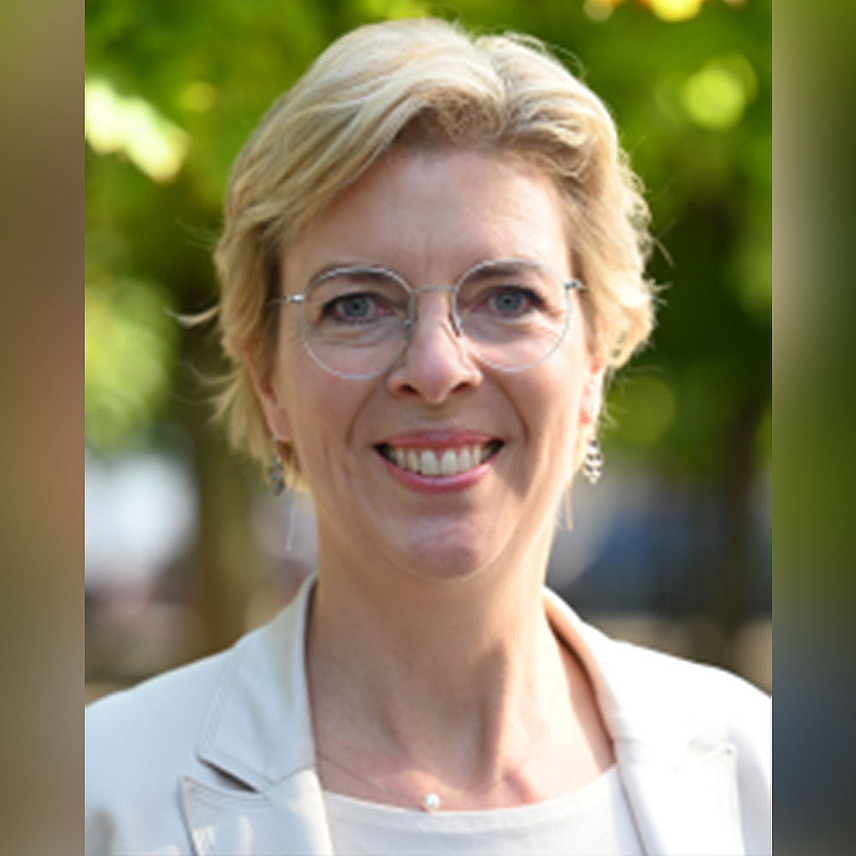 Eine Person mit blonden kurzen Haaren und Brille lächelt in die Kamera