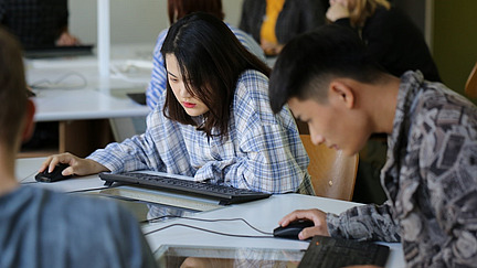 Chinesische Studierende sitzen an PC- Tastatur und PC-Maus