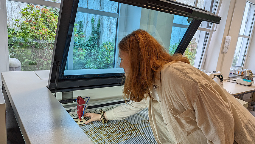 Eine Studentin legt ein Stück Holz in einen Lasercutter