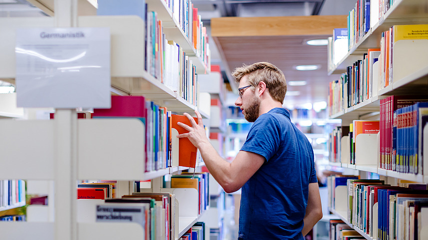 Ein Mann in der Bibliothek Alte Münze zieht ein Buch aus einem Bücherregal.