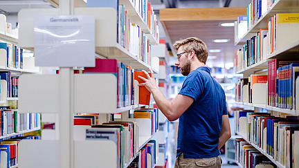 A man in the Alte Münze library pulls a book from a bookshelf.