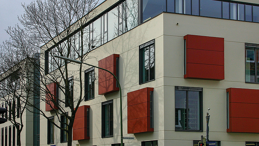 Color photo with a view of the window facade of the building. Some of the windows have dark red cladding.