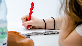 Close-up of a notepad on which a student is taking notes with a red pen.