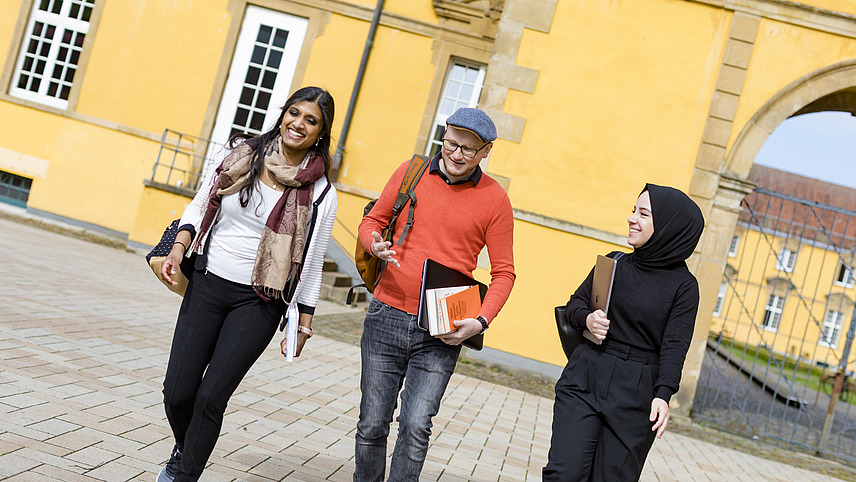 Drei Personen gehen durch den Schlossinnenhof und unterhalten sich.