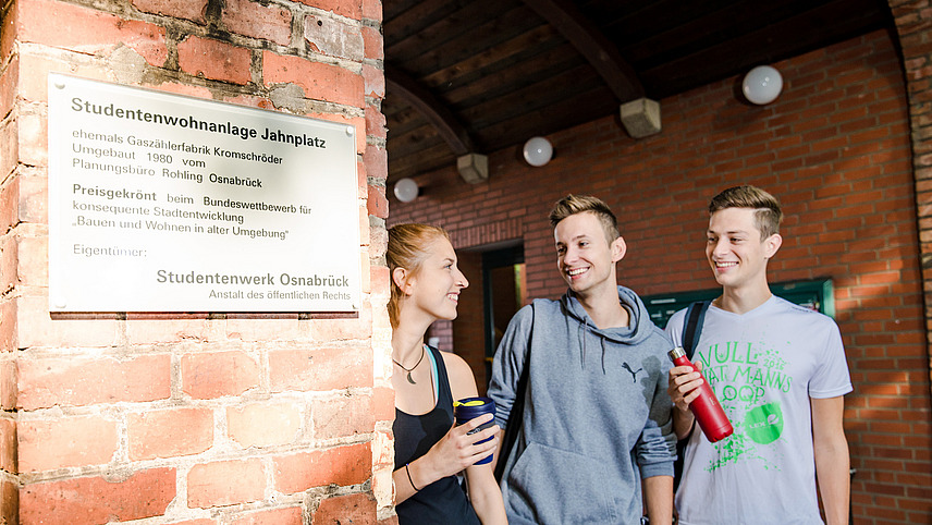 Drei Studierende stehen vor der Eingangstafel der alten Fabrik, einem Studentenwohnheim für rund 300 Personen in Osnabrück.