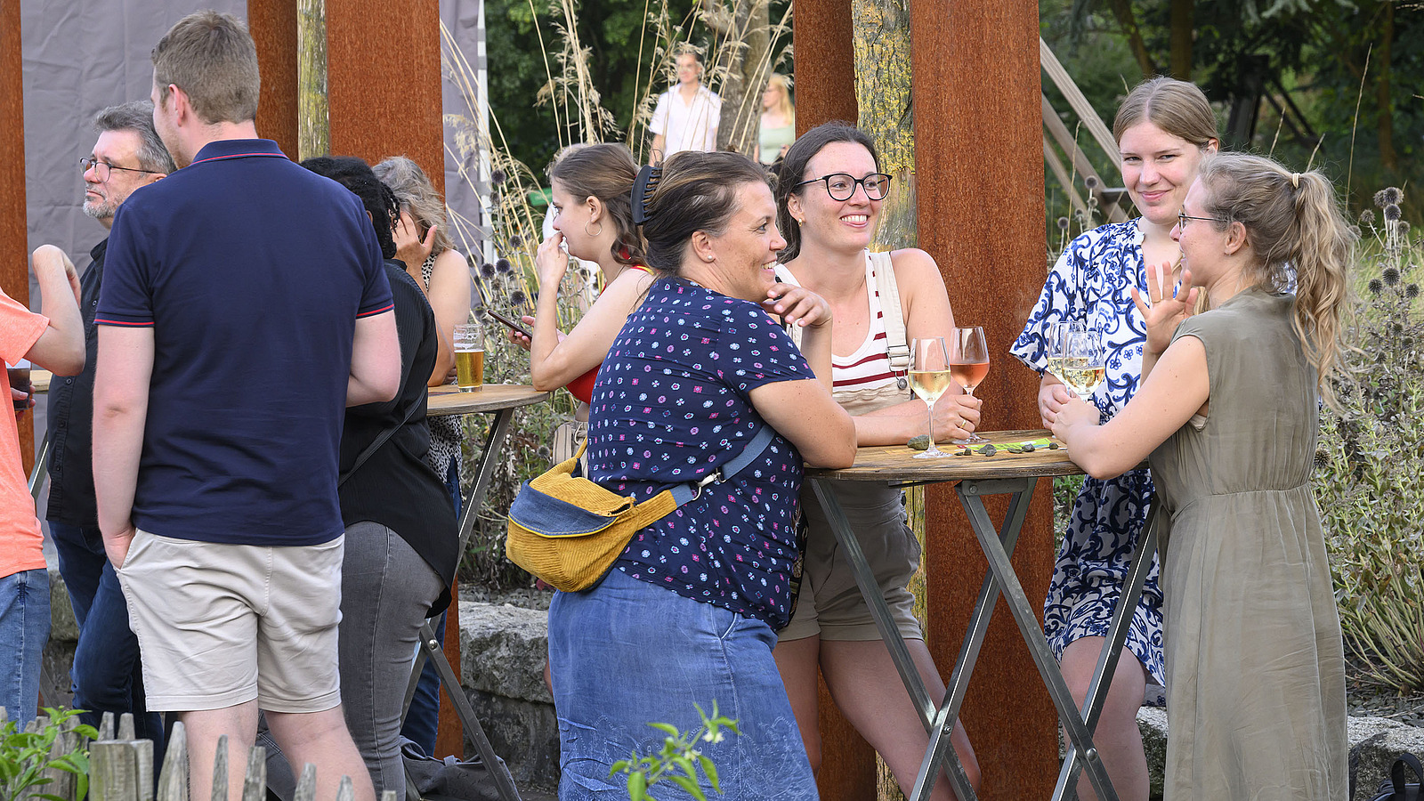 Mehrere fröhliche Personen mit Getränken bei einer Gartenparty.