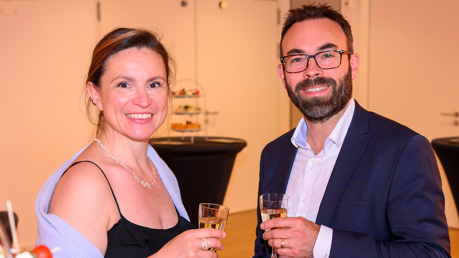 Two festively dressed people with champagne glasses smile into the camera