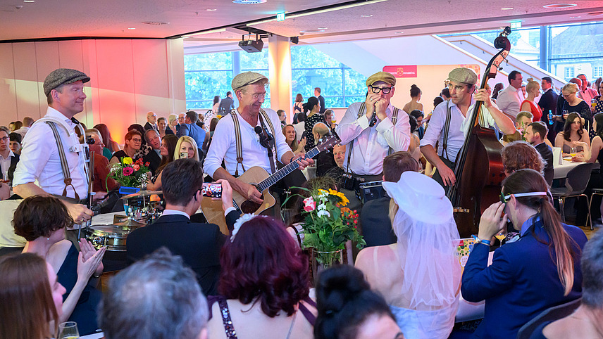 Four musicians play in the midst of standing and seated guests