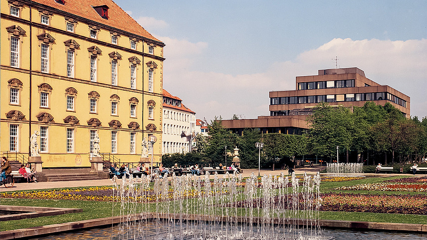 Color photo, taken in the castle garden. The castle front with the old terrace on the left edge of the picture. In the foreground are the fountains and flowerbeds that no longer exist, in the background the EW building with concrete front, without today's cladding.