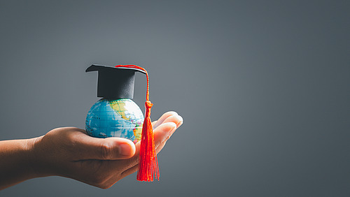 Graduation cap with Earth globe. Concept of global business study, abroad educational, Back to School. Education in Global world, Study abroad business in universities in worldwide. language study Eine Hand hält einen winzigen Globus.