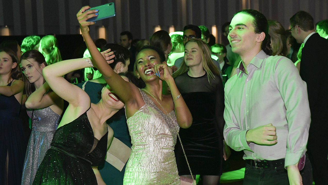 Three festively dressed, smiling students take a selfie on the dance floor.”