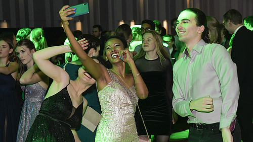 Three festively dressed, smiling students take a selfie on the dance floor.”