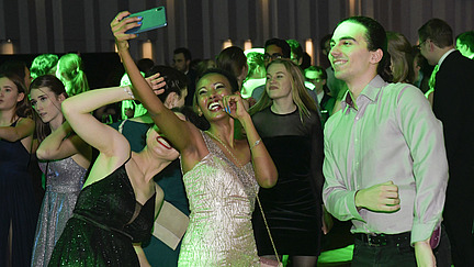 Three festively dressed, smiling students take a selfie on the dance floor.”